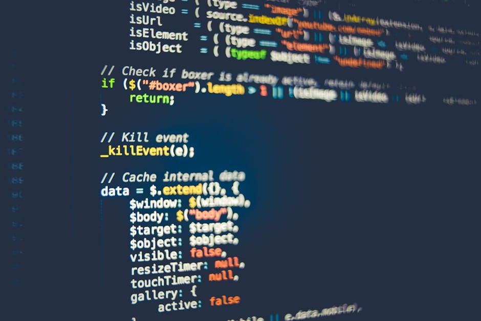 The image shows a person's hand typing on a laptop keyboard placed on a wooden desk. The laptop screen displays lines of code or a website's HTML, with colors indicating different syntax elements. The